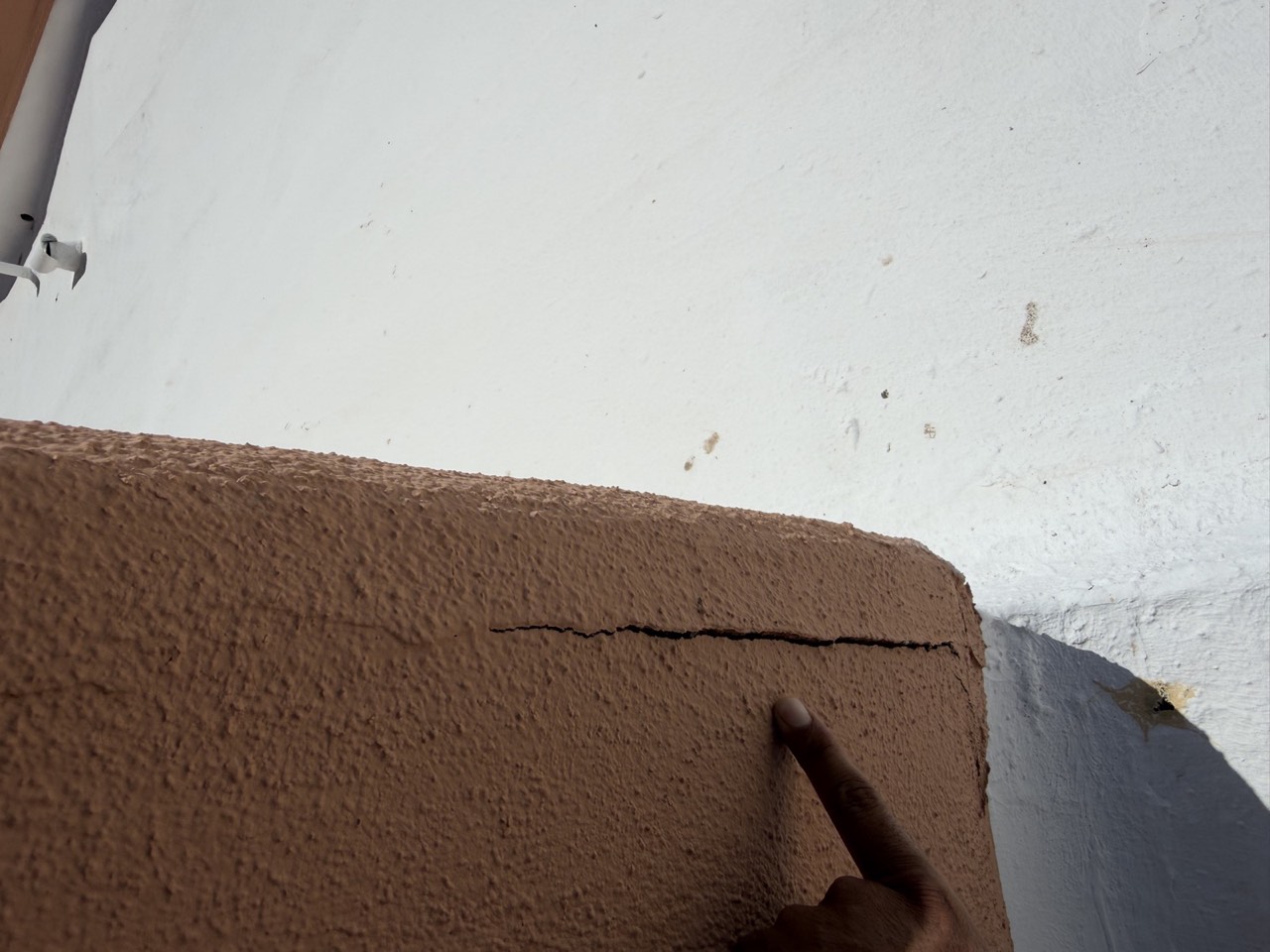 Crack at a roof-to-wall transition where a stucco parapet corner meets a coated flat roof
