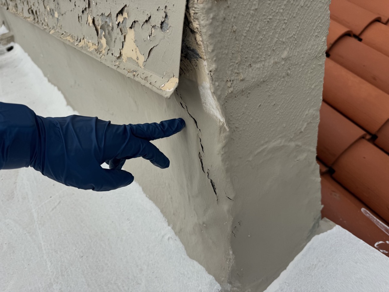 Stucco corner crack at a roof-to-wall transition, where a coated flat roof meets a clay tile roof section